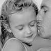 A black-and-white photo of a Dad kissing his daughter's cheek 
