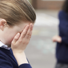 An upset school girl is a victim of bullying, as her peers taunt her in the background