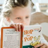 A young girl reading a Doctor Seuss book 