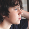 A troubled looking young boy looks out of a window