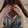 A teenage girl sits sadly with her head in her hands