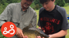 A support worker and a boy holding a large fish, during an outdoor Lads Need Dads fishing activity