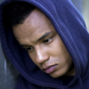 a young man leans against a wall looking downwards while wearing a hoodie.