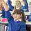 School children in a classroom, putting their hands up