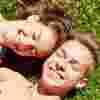 Teenage boy and girl holding hands, smiling, laying on grass together