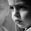 A blank-and-white photo of a troubled young child staring out of a window