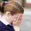 School girl with her face in her hands. Two other girls are bullying her