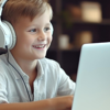 A smiling boy is sat wearing headphones at a laptop computer.
