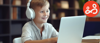 A smiling boy is sat wearing headphones at a laptop computer.